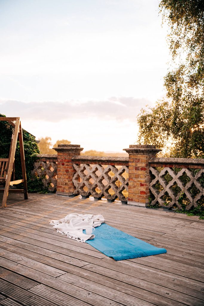 Blaue Yogamatte mit eine Decke und einer Tasse darauf auf einer Holterrasse mit Hollywood-Schaukel im Hintergrund, Gutshaus Pohnstorf